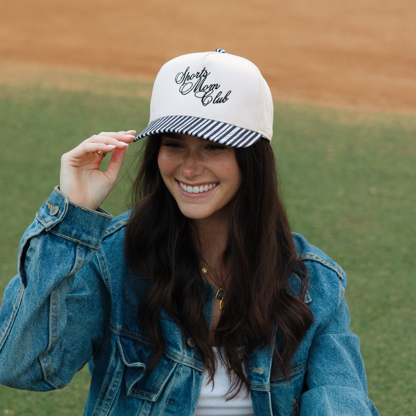 Woman on a baseball field wearing a cap and glove, smiling.