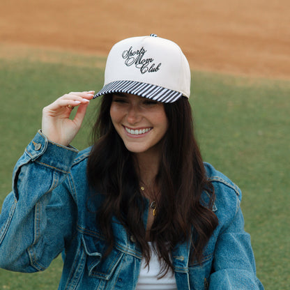 Woman on a baseball field wearing a cap and glove, smiling.